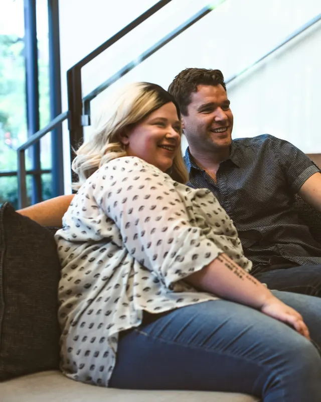 Two people smiling on the sofa, watching the screen