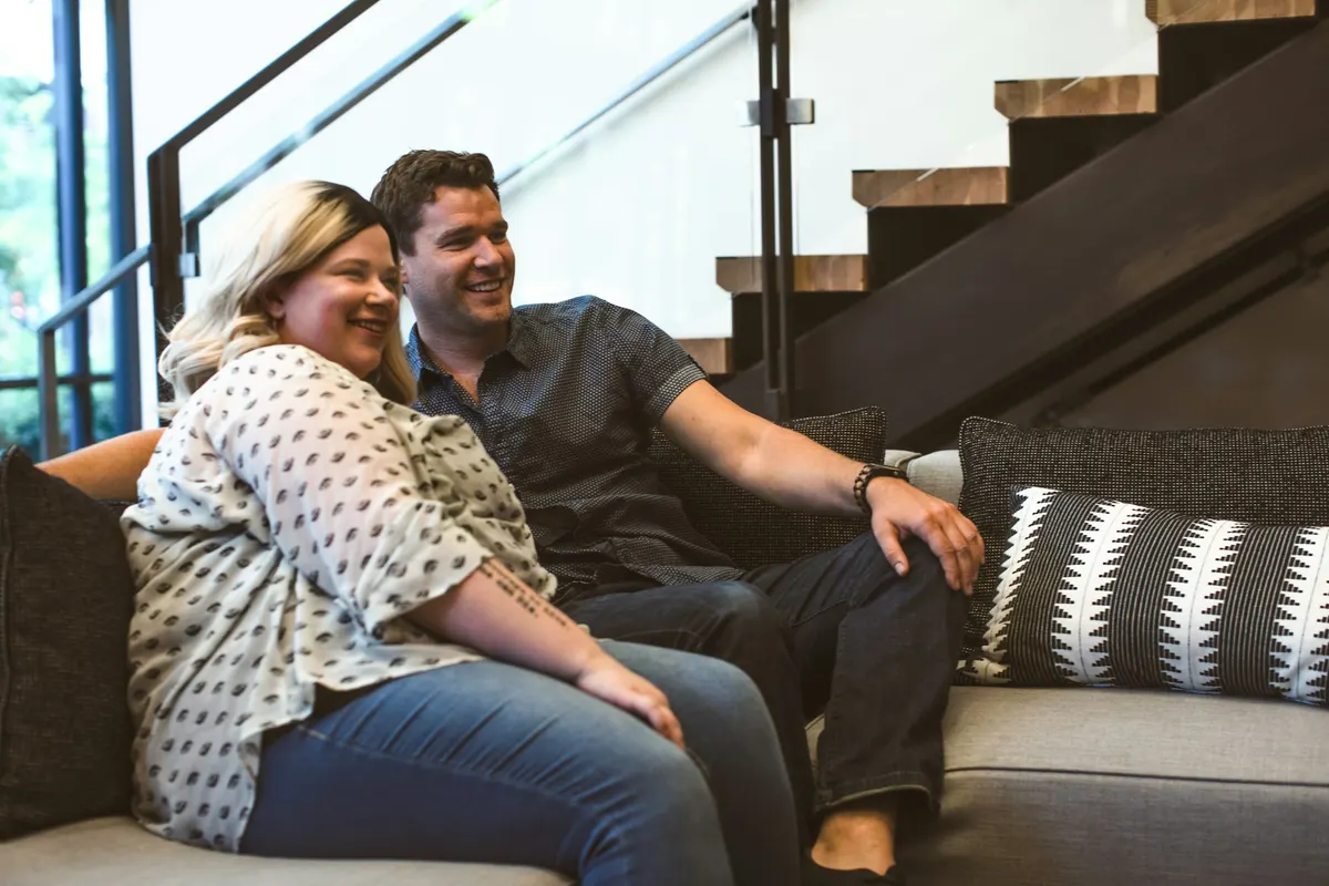 Two people smiling on the sofa, watching the screen